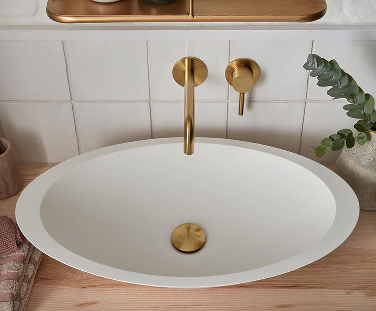 white oval countertop sink with gold brassware